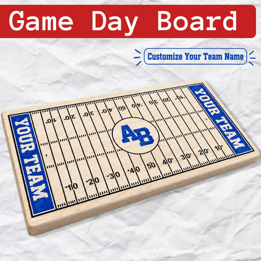 A wooden football field game board with blue end zones, yard lines, and a circular team logo area, shown on a crumpled white paper background. A red banner at the top reads 'Game Day Board' and a blue badge says 'Customize Your Team Name.